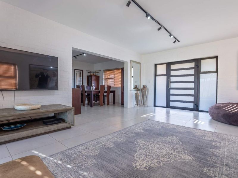 Spacious open-plan living area featuring modern track lighting, neutral tiled flooring, and a distinctive glass-paneled front entrance.