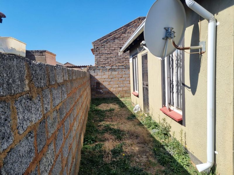 A narrow side or rear exterior passage featuring a boundary wall, security bars on windows, and a satellite dish installation.