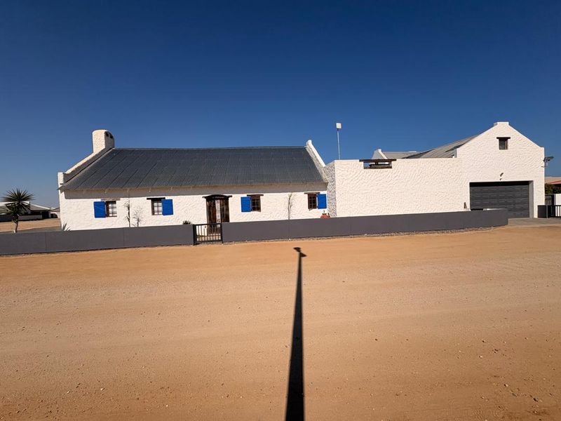 A well-maintained single-story house featuring a white textured facade, blue shutters, a corrugated metal roof, and an integrated garage.
