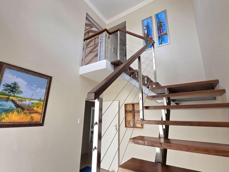 A bright double-volume entrance hallway featuring a modern timber staircase with stainless steel and wire balustrades.