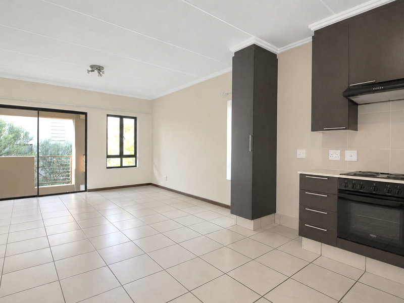 An open-plan living and kitchen area featuring neutral tiled flooring, modern dark cabinetry, built-in appliances, and a sliding door leading to a balcony.