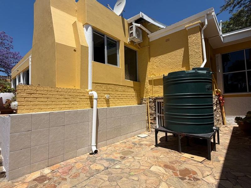 Rear exterior view of the property featuring a stone paved patio, a water storage tank, and a prominent chimney stack.