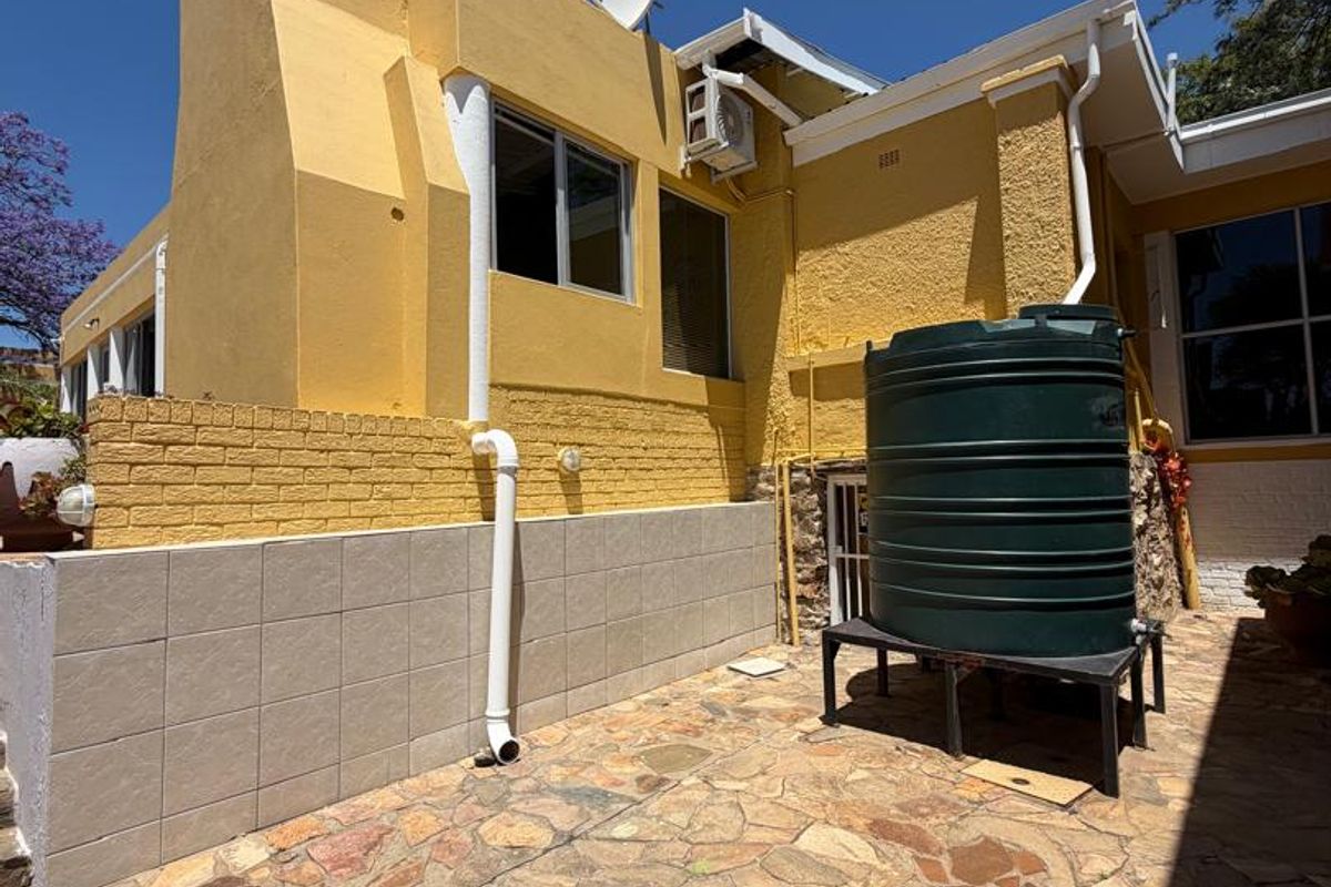 Rear exterior view of the property featuring a stone paved patio, a water storage tank, and a prominent chimney stack.