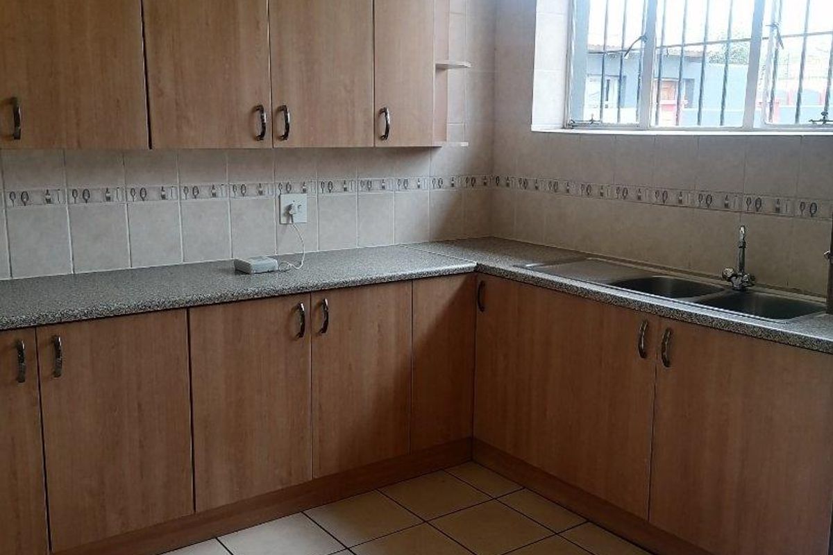 A functional kitchen featuring laminate cabinetry, granite-look countertops, a double bowl stainless steel sink, and ceramic tile flooring.