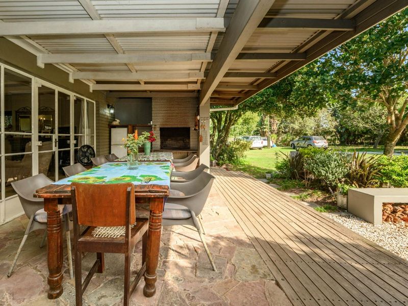 Spacious covered patio featuring stone paving, timber decking, and a built-in braai, providing a functional outdoor entertainment area overlooking the garden.