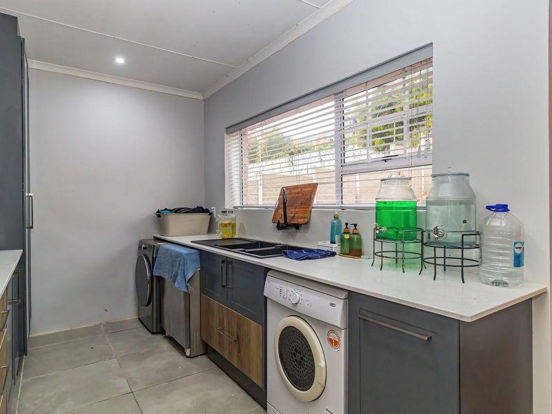 A functional laundry room featuring modern dark cabinetry, stone countertops, an undermount sink, and tiled flooring with ample space for appliances.