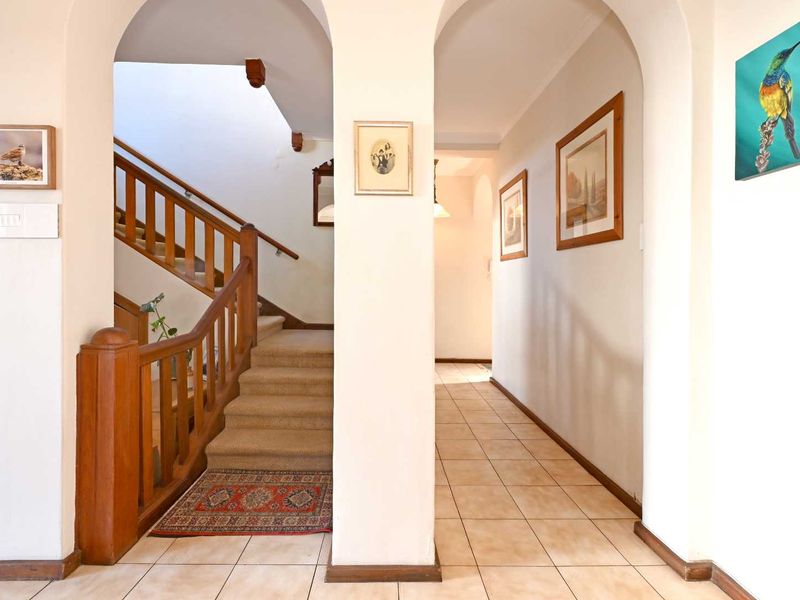 A bright and welcoming hallway featuring tiled flooring, arched architectural details, and a classic wooden staircase leading to the upper level.