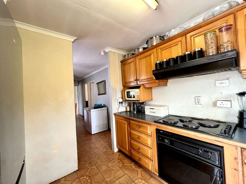 A functional kitchen featuring wooden cabinetry, a built-in oven, and an electric hob, leading into a hallway area with tiled flooring throughout.