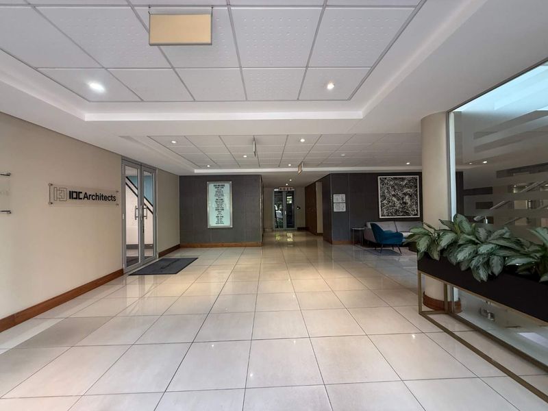 A professional office building lobby featuring polished tiled flooring, a suspended ceiling with recessed lighting, and a glass entrance door.
