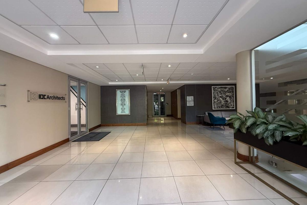A professional office building lobby featuring polished tiled flooring, a suspended ceiling with recessed lighting, and a glass entrance door.
