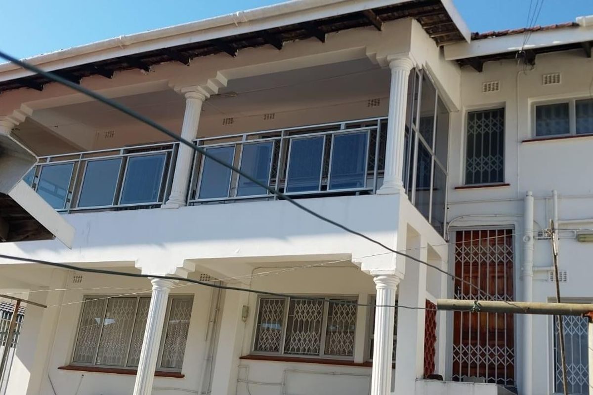Rear elevation of a two-story house featuring a covered balcony with columns, security gates, and sliding windows.