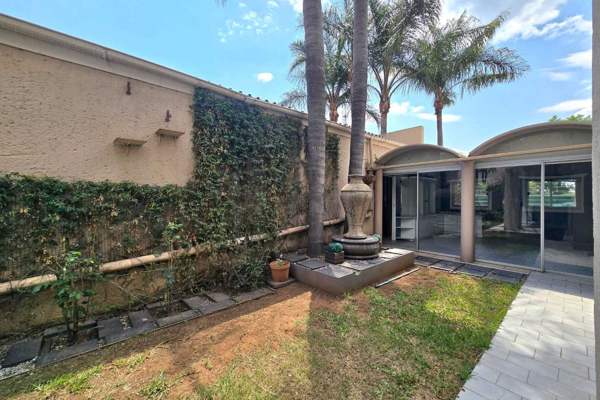 A private rear garden featuring a tiled walkway, stone fountain, and large sliding glass doors providing access to the home's interior living spaces.