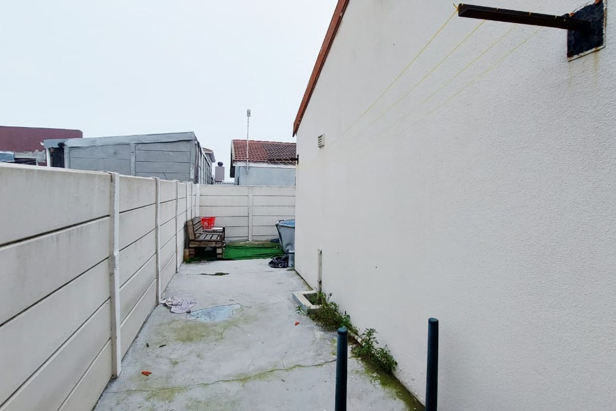 A narrow side exterior area featuring concrete paving, a precast concrete boundary wall, and a wall-mounted clothesline fixture.