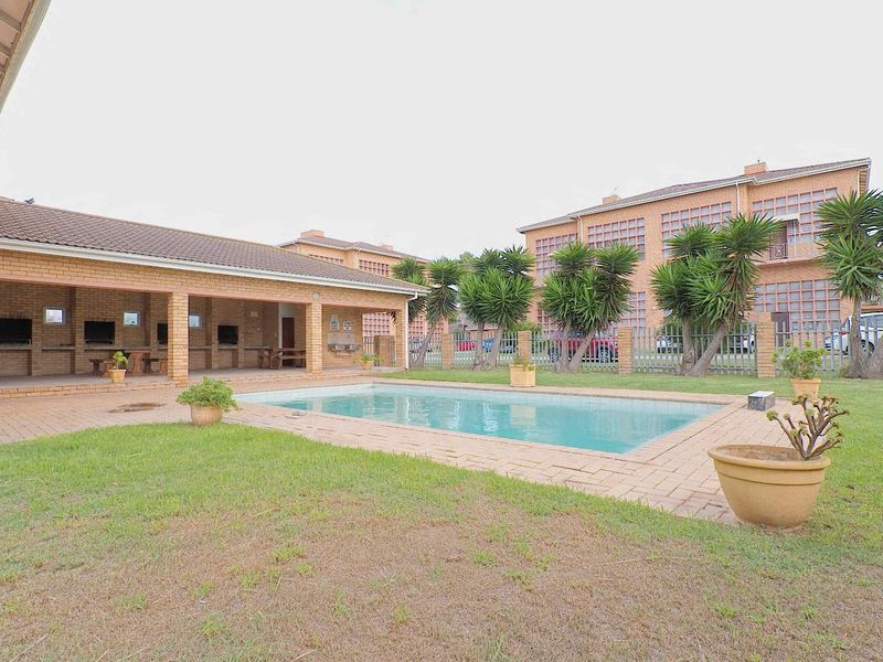 Outdoor pool area featuring a swimming pool, a covered brick entertainment space with built-in braai facilities, and a landscaped garden setting.