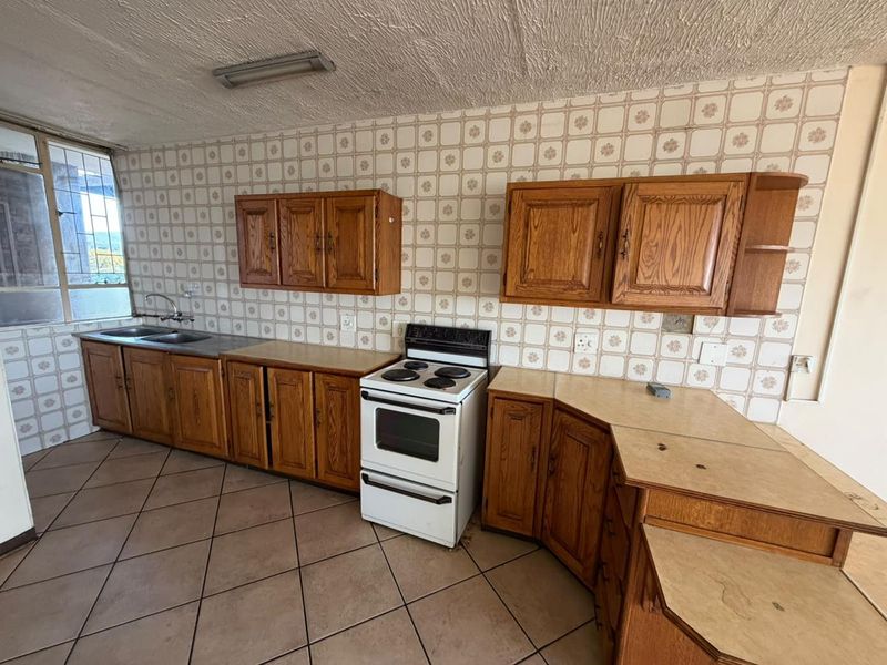 A dated kitchen featuring wooden cabinetry, laminate countertops, a double basin sink, and a freestanding stove, finished with ceramic wall and floor tiles.