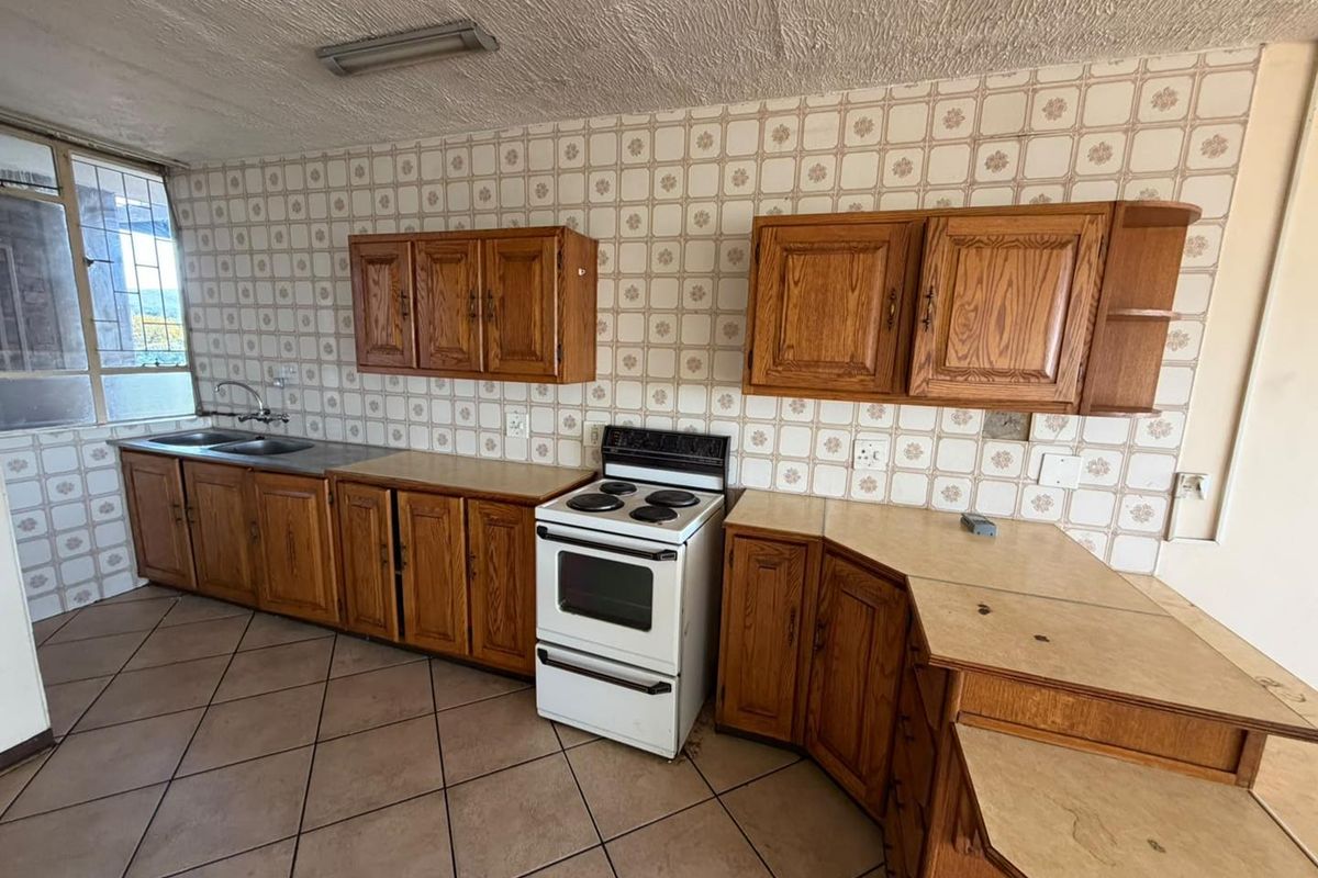 A dated kitchen featuring wooden cabinetry, laminate countertops, a double basin sink, and a freestanding stove, finished with ceramic wall and floor tiles.