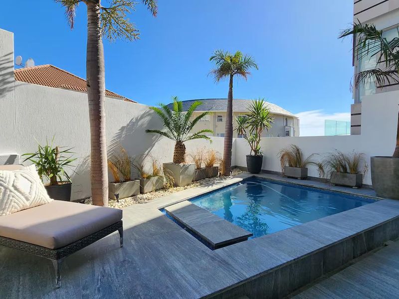 A private outdoor pool area featuring stone tile paving, a compact swimming pool, and established palm trees within a walled courtyard setting.