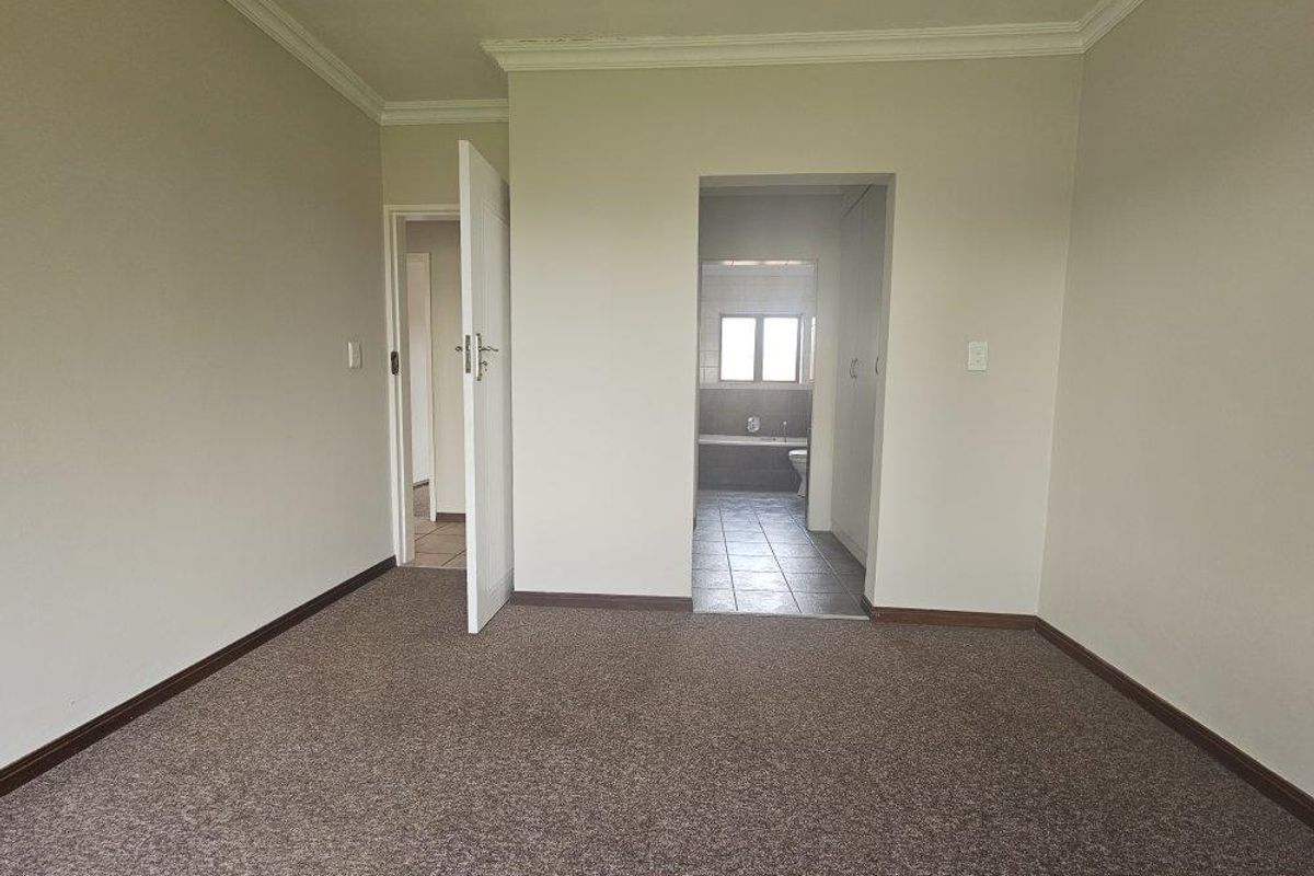 An empty bedroom featuring neutral walls, carpet flooring, and direct access to an en-suite bathroom.