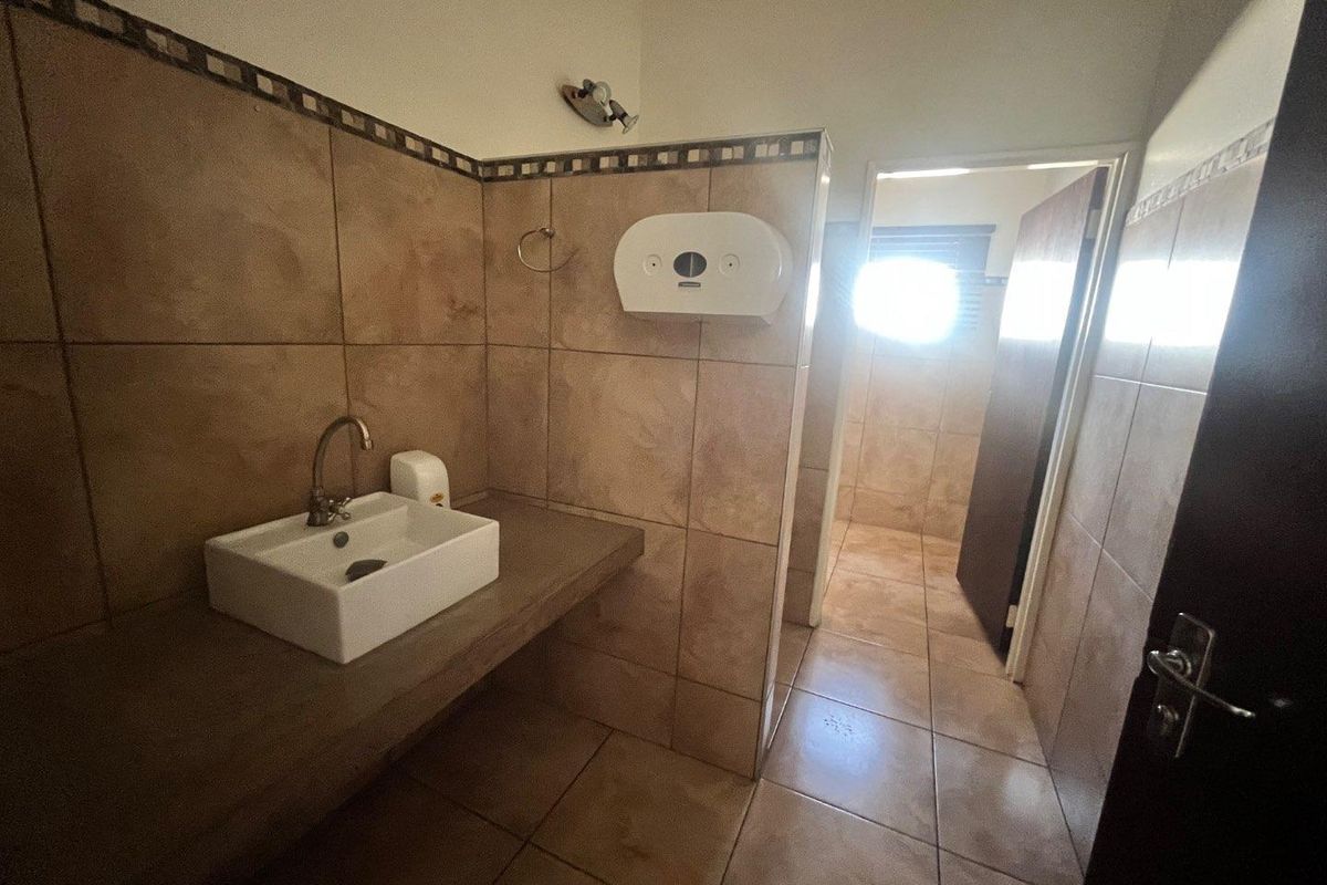 A functional commercial bathroom featuring tiled walls and floors, a vessel sink mounted on a concrete vanity, and a paper towel dispenser.