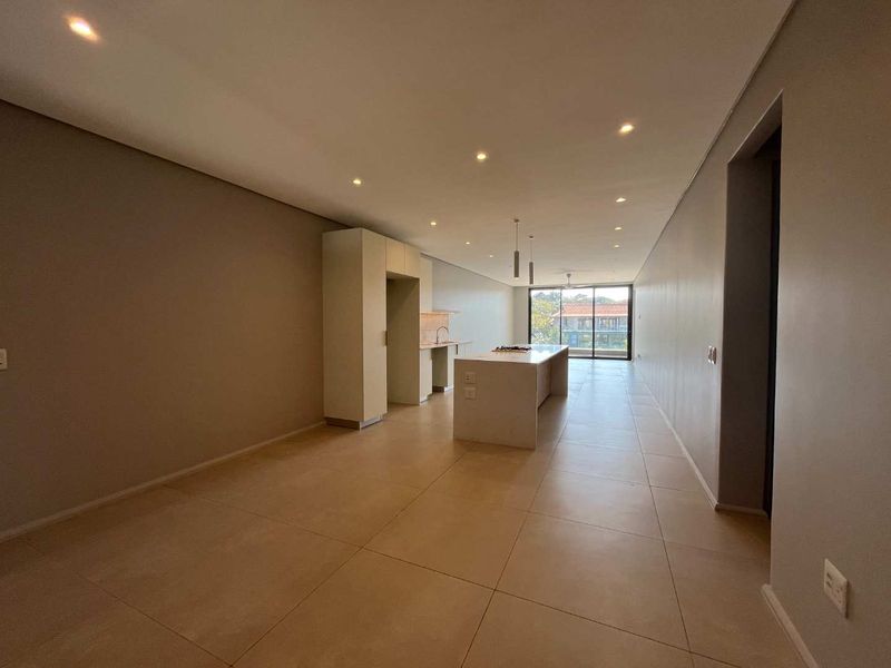 Spacious open-plan living and kitchen area featuring modern cabinetry, a central island with a hob, tiled flooring, and large sliding doors leading to a balcony.