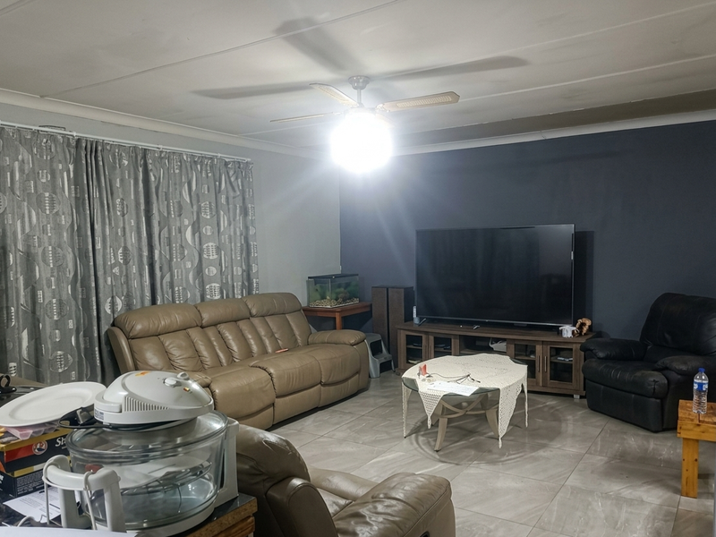 A living room featuring large format floor tiles, a central ceiling fan, and a dark blue accent wall.