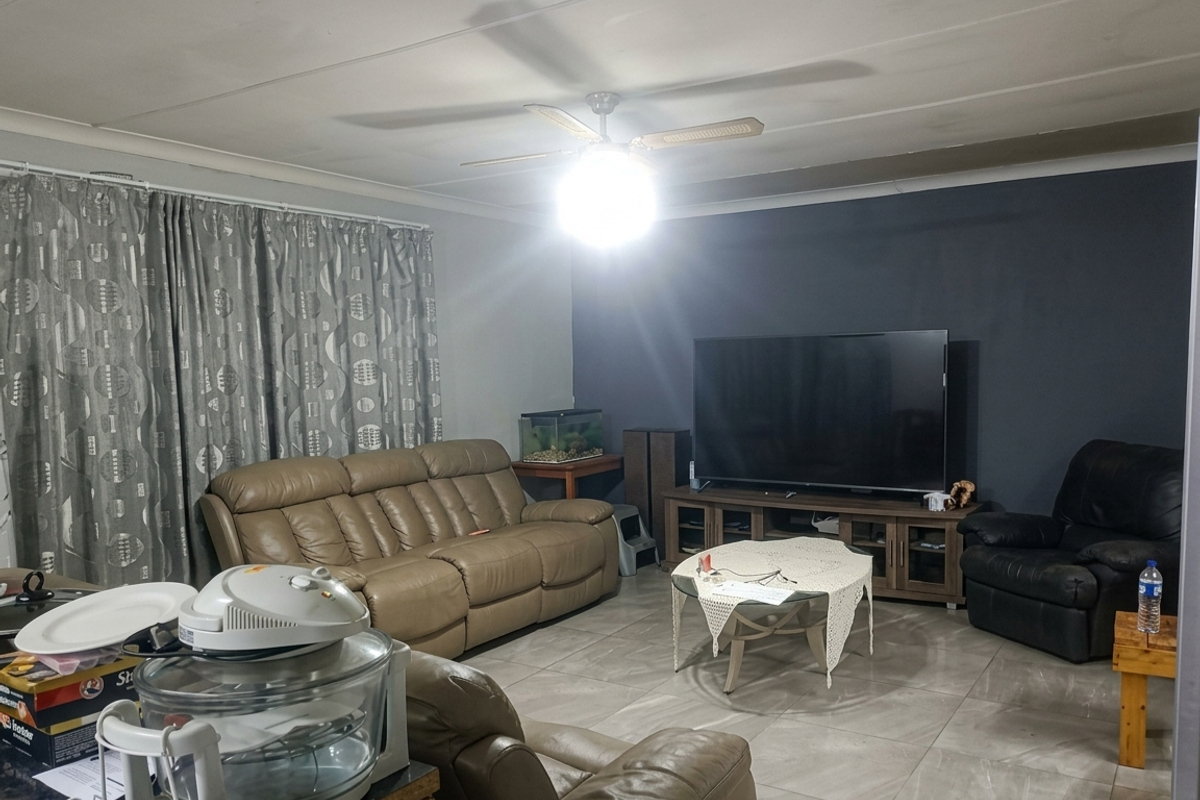 A living room featuring large format floor tiles, a central ceiling fan, and a dark blue accent wall.