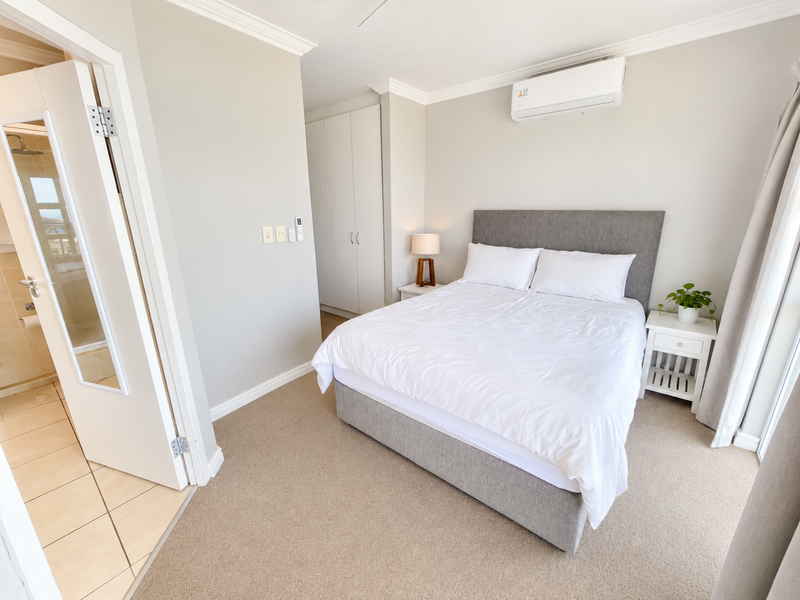 A well-maintained bedroom featuring neutral carpeting, built-in cupboards, a wall-mounted air conditioning unit, and direct access to an en-suite bathroom.