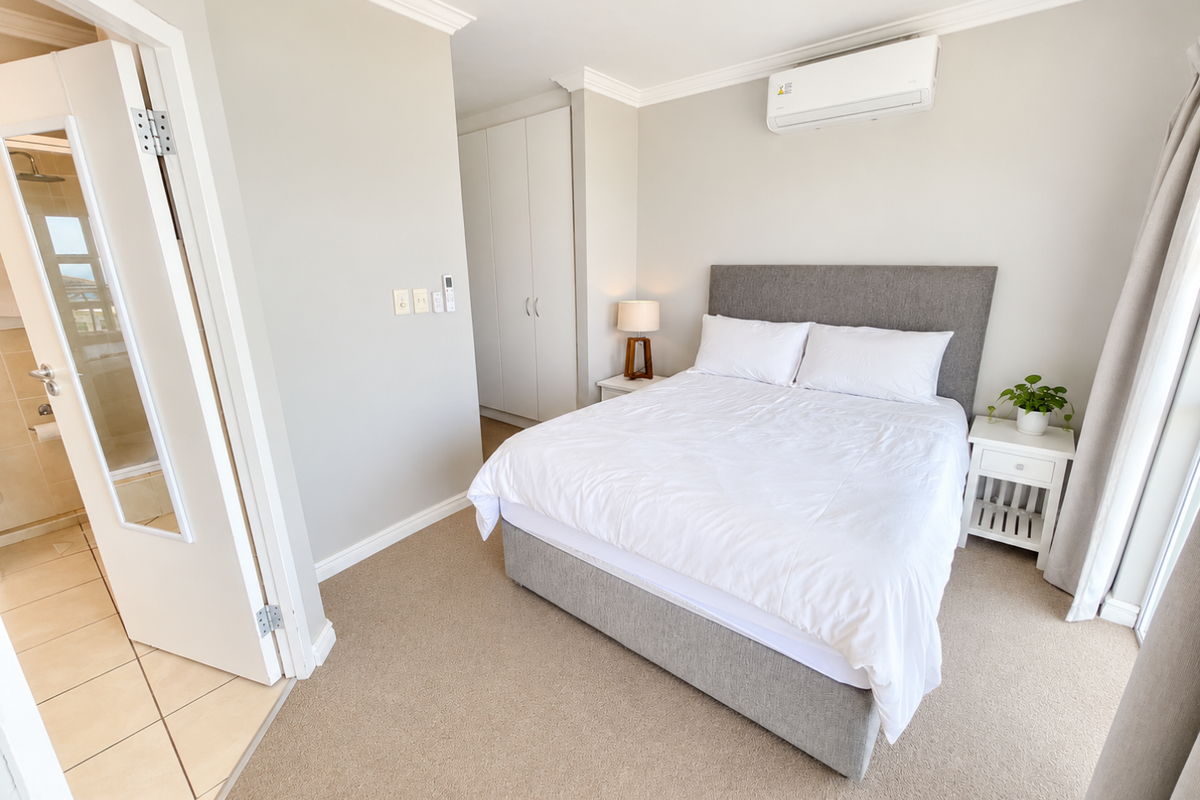 A well-maintained bedroom featuring neutral carpeting, built-in cupboards, a wall-mounted air conditioning unit, and direct access to an en-suite bathroom.