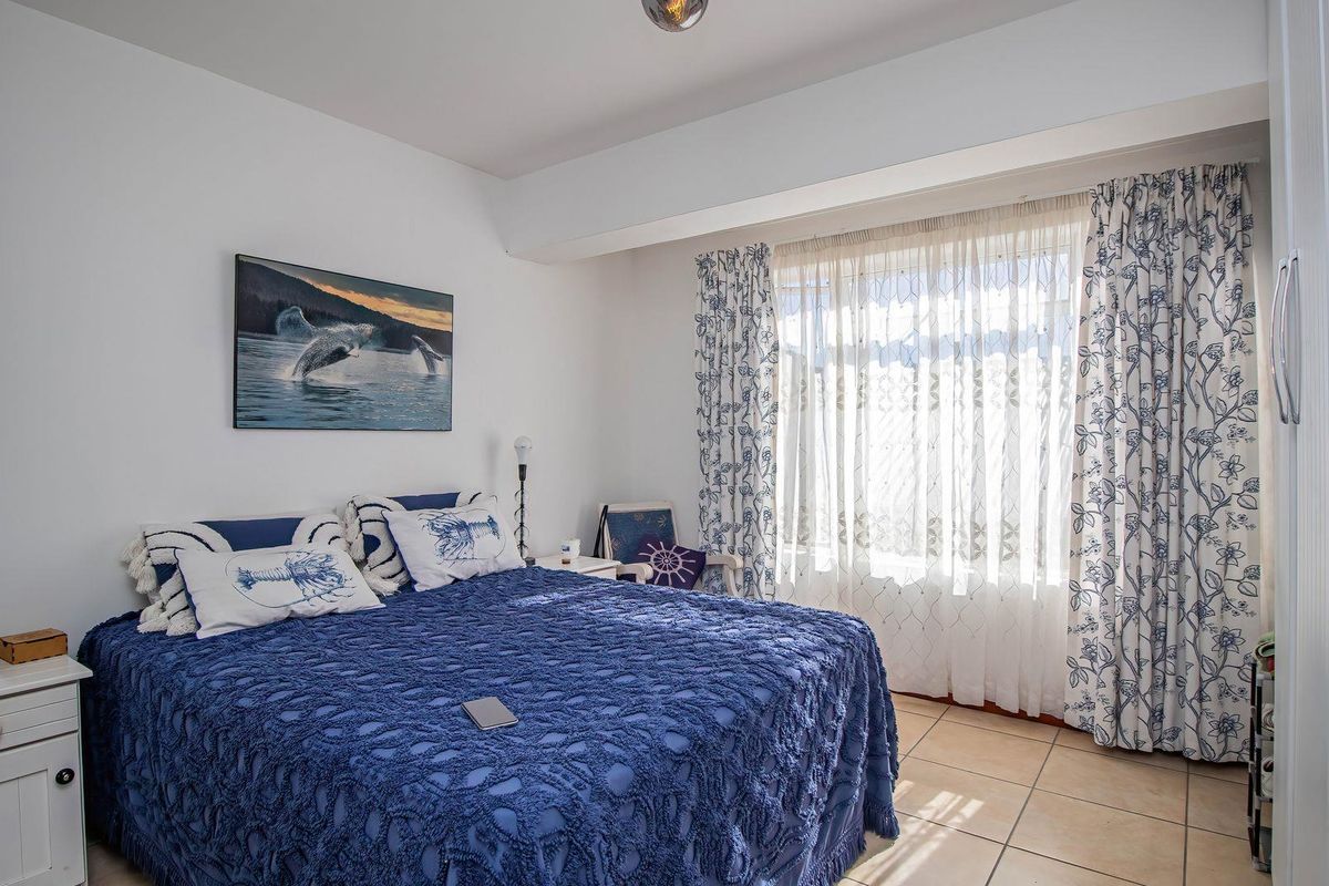 A well-lit bedroom featuring tiled flooring, a built-in wardrobe, and large windows with curtains, providing a comfortable and functional living space.