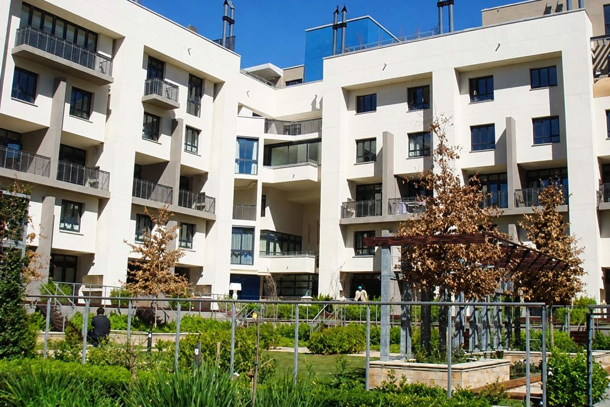 A view of the apartment complex rear facade featuring modern architecture, private balconies, and a well-maintained communal garden area with a pergola.