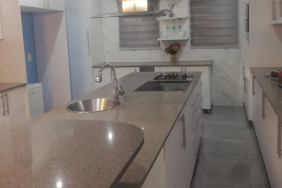 Modern kitchen featuring a large central island with a built-in hob, sink, and stone countertops, complemented by sleek cabinetry and tiled flooring.