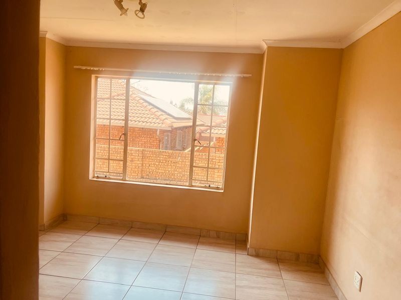 An empty bedroom featuring tiled flooring and a large window, providing a blank canvas for potential interior design updates.
