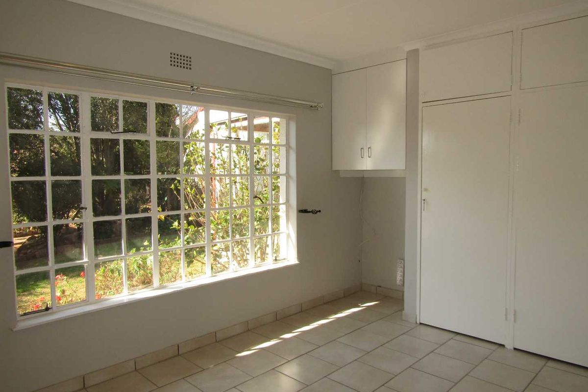A bright, empty bedroom featuring large grid-style windows, built-in white cabinetry, and tiled flooring, offering a clean and neutral space.