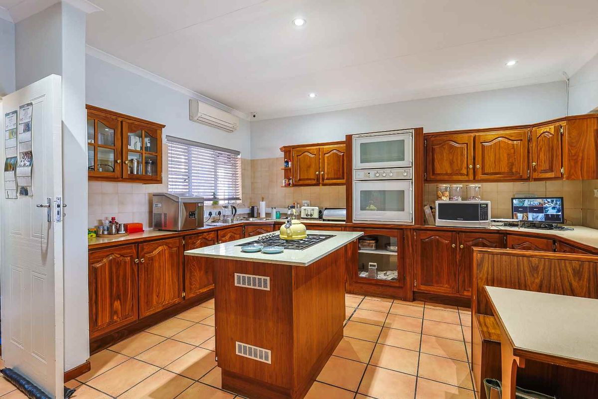 Spacious kitchen featuring traditional timber cabinetry, a central island with built-in gas hob, wall-mounted oven, and tiled flooring throughout.