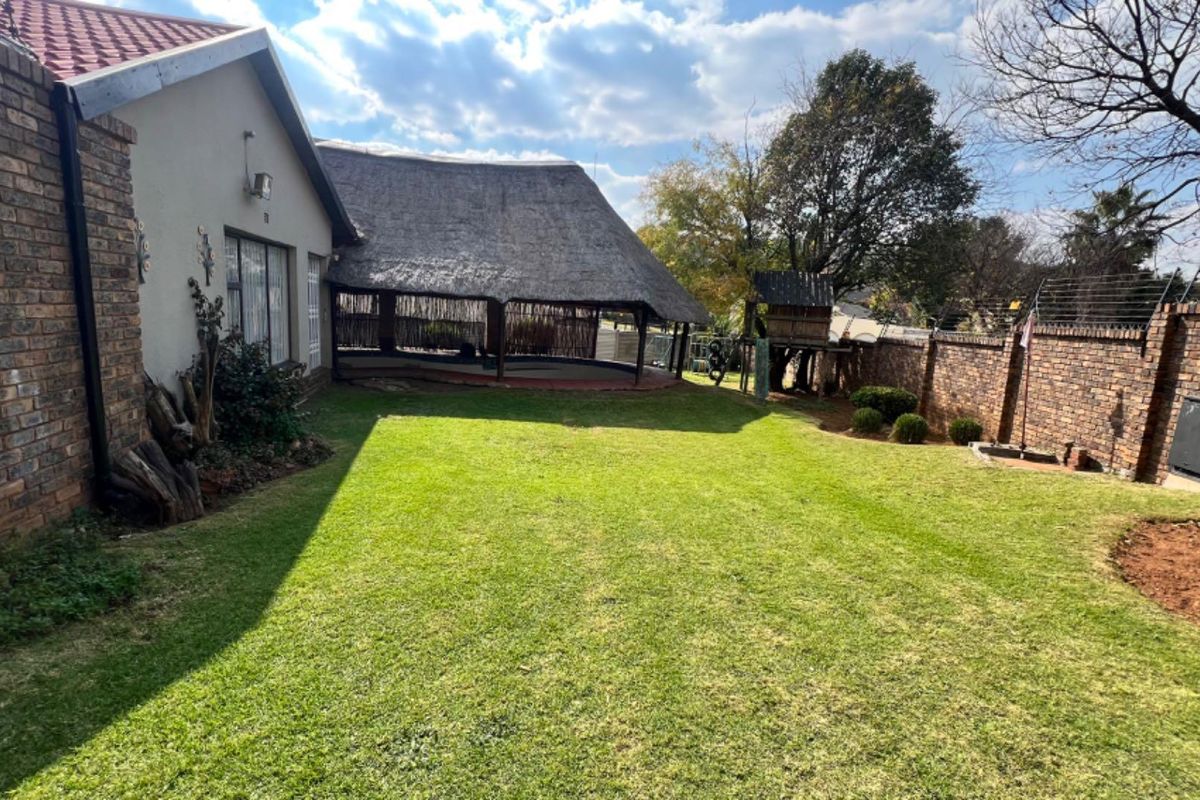 Spacious rear garden featuring a large lawn, perimeter brick walling, and a covered thatched patio area suitable for outdoor entertaining.