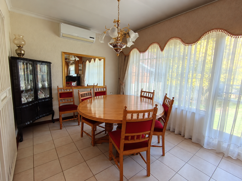 A dining room featuring tiled flooring, a split-system air conditioner, and a large window with a decorative pelmet, providing ample natural light.