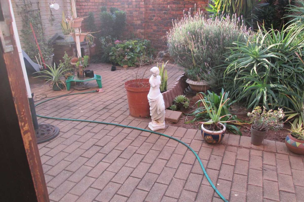 A private rear courtyard featuring brick paving and established garden beds enclosed by a brick boundary wall.