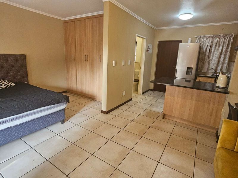 Open-plan studio apartment featuring tiled flooring, built-in bedroom cupboards, and a compact kitchen area with granite countertops.