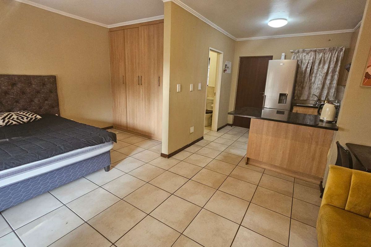 Open-plan studio apartment featuring tiled flooring, built-in bedroom cupboards, and a compact kitchen area with granite countertops.