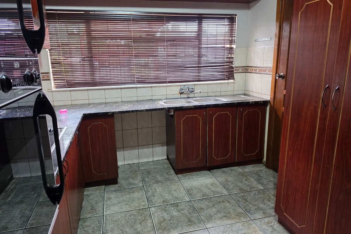 A functional kitchen featuring dark wood-finish cabinetry, laminate countertops, a double-basin sink, and tiled flooring with a large window providing natural light.