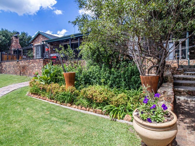 A well-maintained rear garden featuring a brick paved pathway, stone stairs, and a raised patio area with a brick chimney and wrought iron railings.