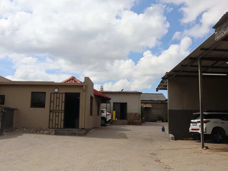 Exterior view of the office property featuring a paved courtyard, multiple building structures, and a covered carport area.