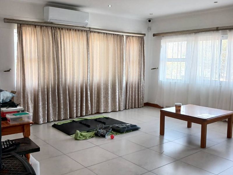 Spacious living area featuring neutral tiled flooring, recessed downlighting, and a wall-mounted air conditioning unit.