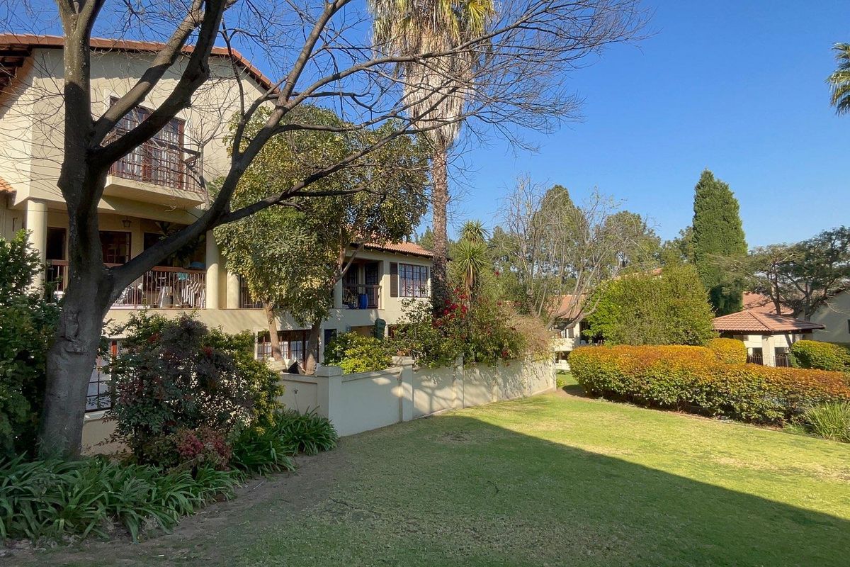 A view of the rear apartment building facade featuring balconies, a well-maintained lawn, and established garden landscaping.