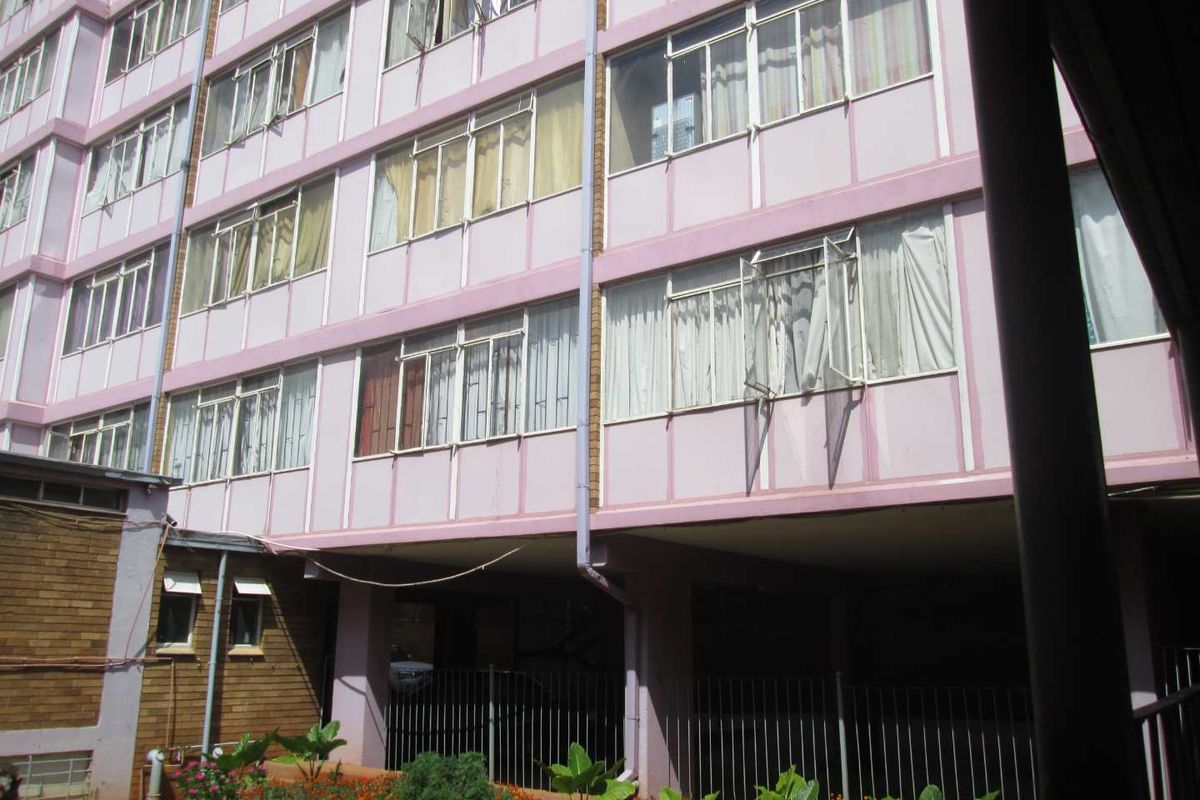 Exterior view of a multi-story apartment building facade featuring metal-framed windows and ground-level parking area.