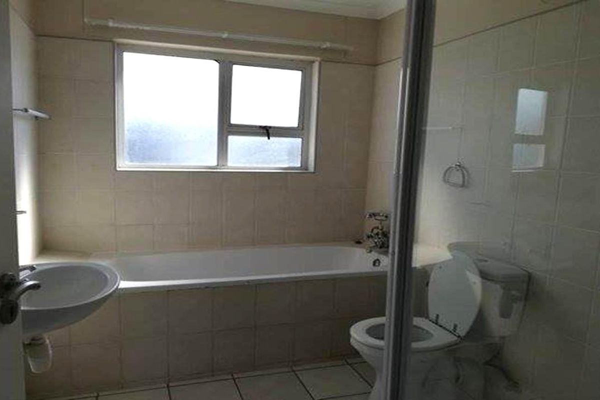 A functional bathroom featuring a built-in bathtub, pedestal basin, and toilet, finished with neutral wall tiles and tiled flooring.
