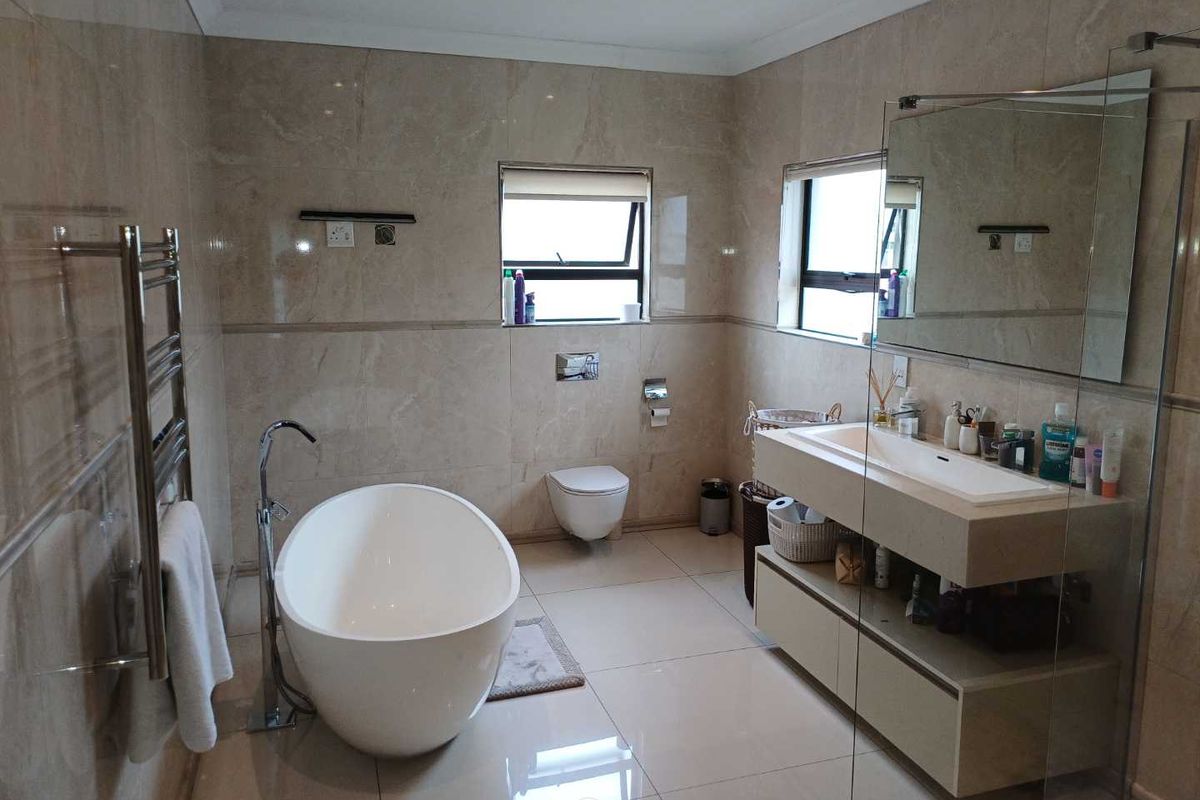 Modern, well-appointed bathroom featuring a sleek freestanding bathtub, wall-mounted toilet, floating vanity with integrated basin, and high-quality floor-to-ceiling tiling.
