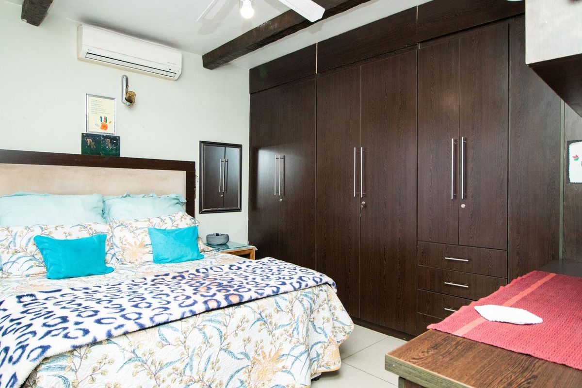 A well-maintained bedroom featuring extensive dark wood built-in cabinetry, exposed ceiling beams, and a wall-mounted air conditioning unit.