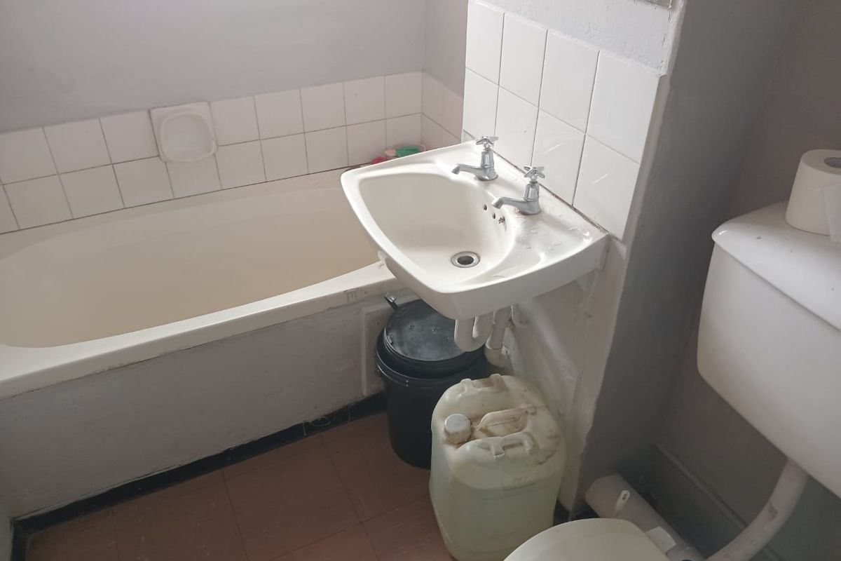 A dated bathroom featuring a standard bathtub, wall-mounted basin, and toilet with basic tiled splashbacks and flooring.