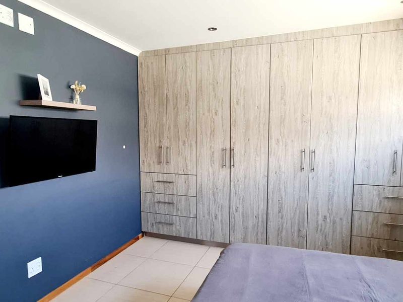 A well-maintained bedroom featuring extensive built-in cupboards with wood-grain finish, dark blue accent wall, and neutral tiled flooring.